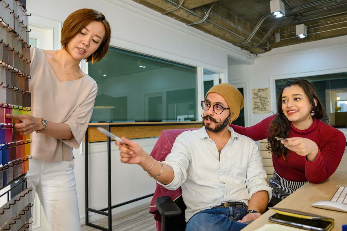 Trois individus dans un espace de travail, une présente des teintes, une autre tient un objet, une troisième regarde attentivement Trois individus dans un espace de travail, une présente des teintes, une autre tient un objet, une troisième regarde attentivement