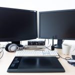 Bureau avec deux moniteurs noirs, ordinateur portable, claviers, souris et enceintes de monitoring