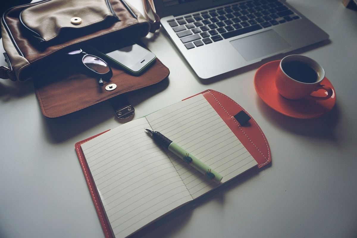 Un ordinateur portable, une tasse de café sur une soucoupe, un agenda ouvert avec un stylo, et un portefeuille sur une table Un ordinateur portable, une tasse de café sur une soucoupe, un agenda ouvert avec un stylo, et un portefeuille sur une table