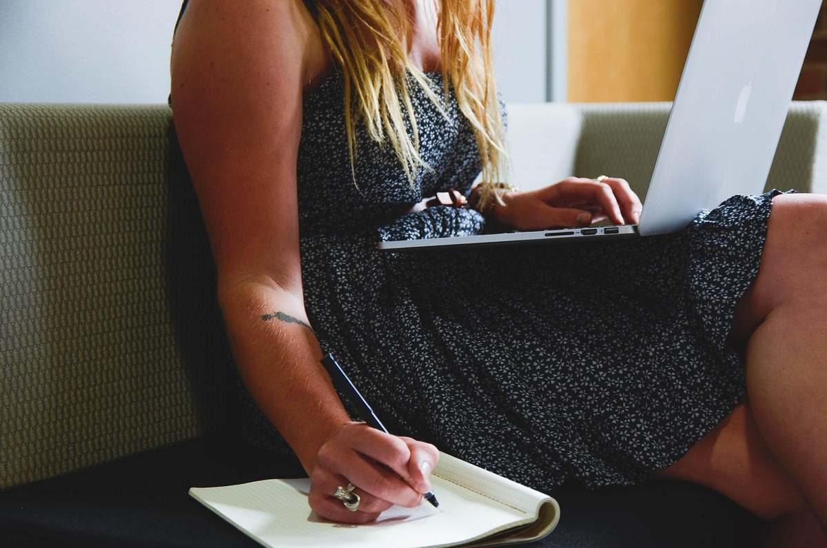 Femme assise, carnet à la main, ordinateur sur les genoux, vêtement noir et blanc Femme assise, carnet à la main, ordinateur sur les genoux, vêtement noir et blanc