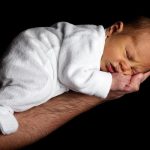 Un bébé endormi reposant sa tête sur la main d'un adulte