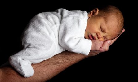 Un bébé endormi reposant sa tête sur la main d'un adulte
