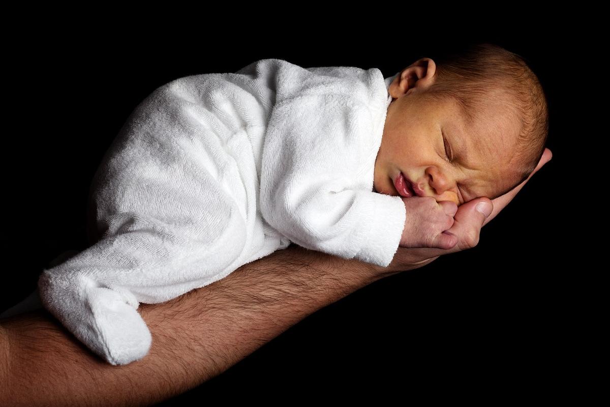 Un bébé endormi reposant sa tête sur la main d'un adulte