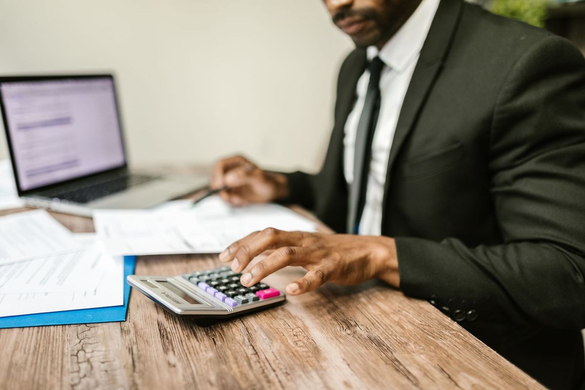 Homme en costume, calculatrice, stylo, ordinateur portable, papiers sur un bureau en bois Homme en costume, calculatrice, stylo, ordinateur portable, papiers sur un bureau en bois