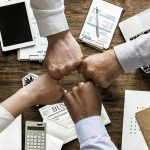 Quatre mains jointes au-dessus d'un bureau avec ordinateurs, documents et fournitures de travail