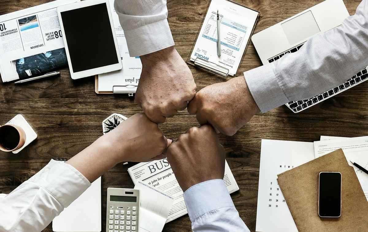 Quatre mains jointes au-dessus d'un bureau avec ordinateurs, documents et fournitures de travail