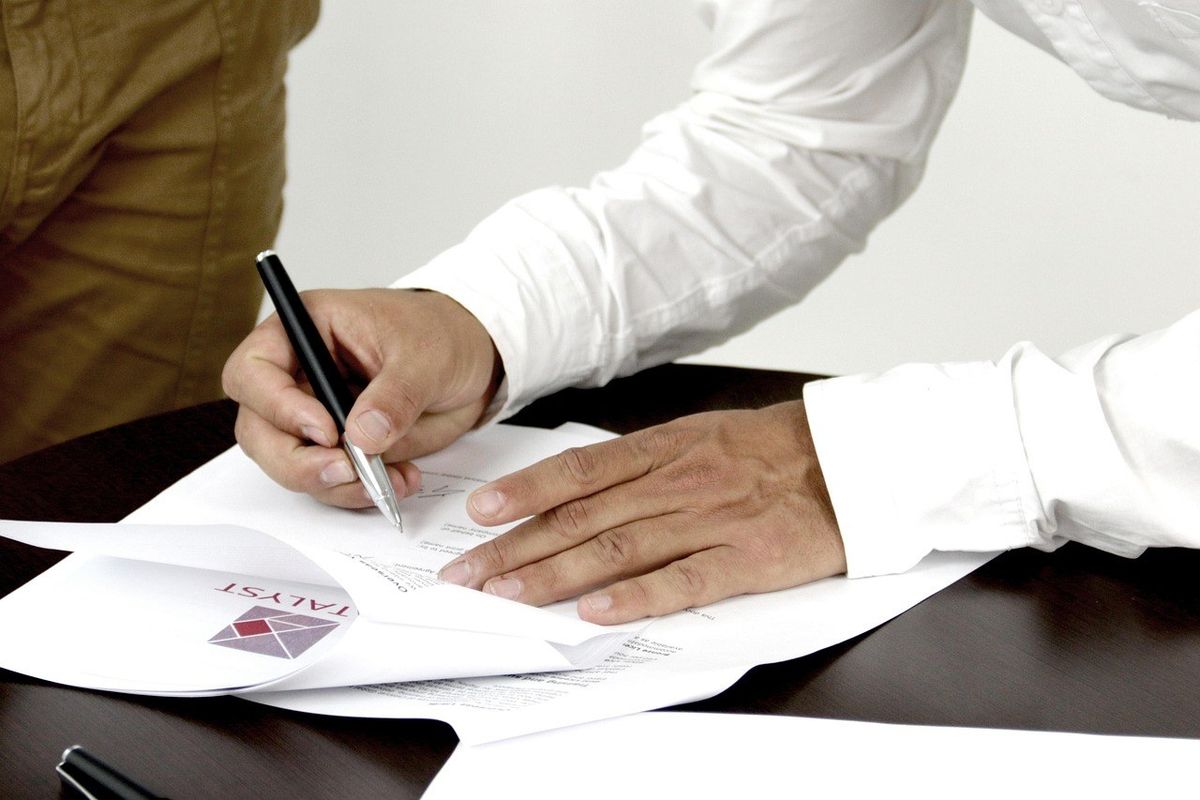 Main écrivant sur un document avec un stylo, une autre main posée dessus Main écrivant sur un document avec un stylo, une autre main posée dessus