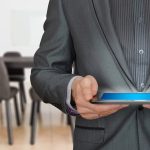 Homme en costume noir tenant une tablette lumineuse dans une salle de réunion