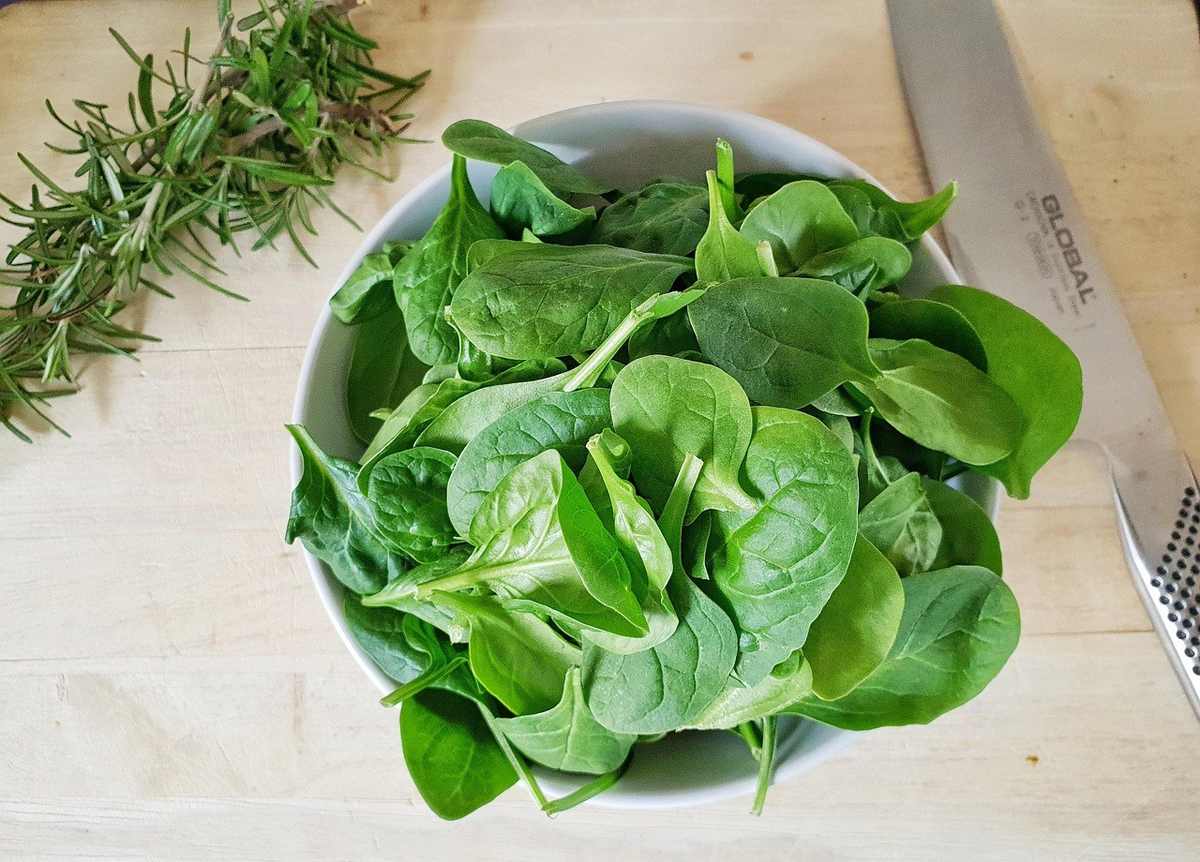 Salade verte dans un bol sur une planche à découper, aiguille de romarin et couteau à côté