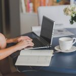 Femme travaille à distance, écrit dans cahier, tasse et fleurs à côté
