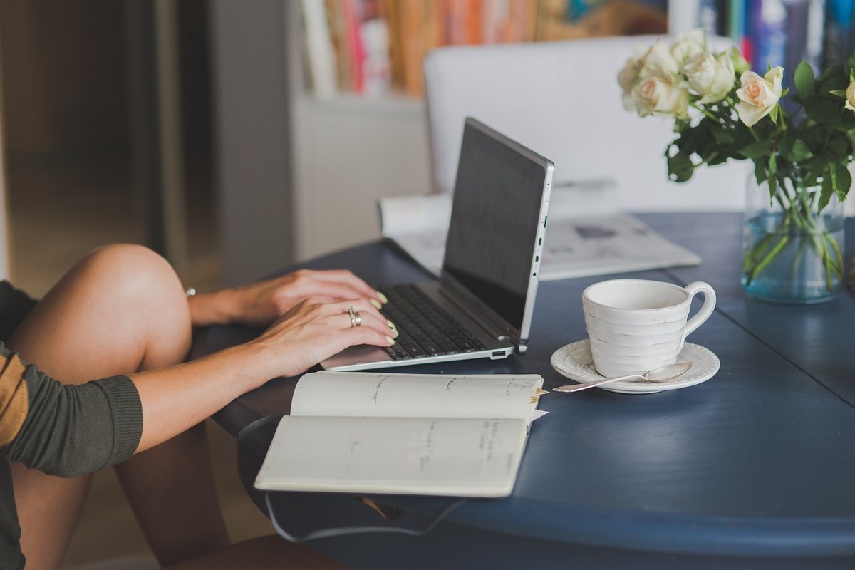 Femme travaille à distance, écrit dans cahier, tasse et fleurs à côté