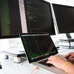 Développeur travaillant sur ordinateur portable avec trois écrans affichant du code informatique
