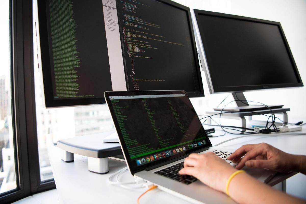 Développeur travaillant sur ordinateur portable avec trois écrans affichant du code informatique