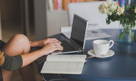 Une femme travaille sur ordinateur avec une tasse de café et des fleurs