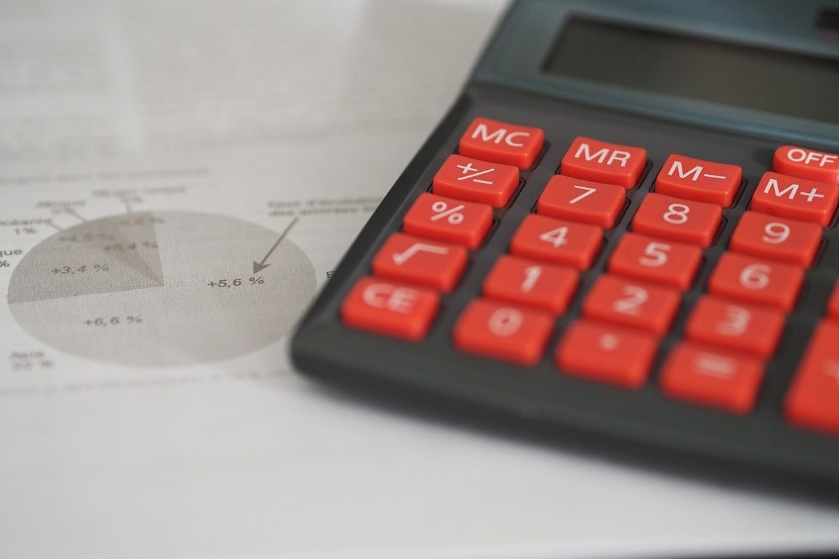 Calculatrice aux touches rouges posée sur des documents comptables avec graphiques et pourcentages visibles