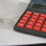 Calculatrice aux touches rouges posée sur des documents comptables avec graphiques et pourcentages visibles