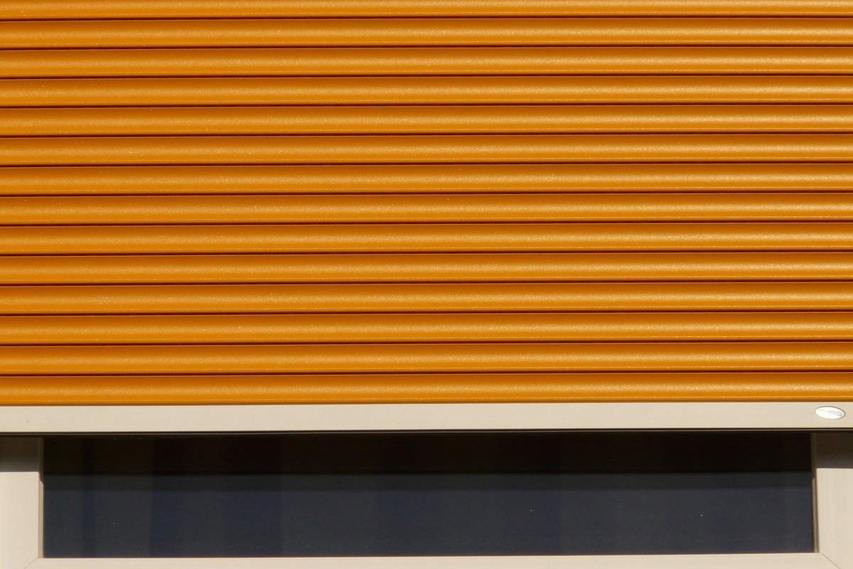 Volet roulant orange partiellement déroulé devant une fenêtre sombre